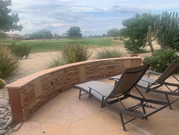 An outdoor patio with stone walls and two lounge chairs.