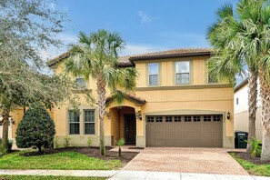 A two-story house with a garage, surrounded by palm trees and a well-maintained lawn. - Disney 9BR Villa: Arcade, 2 Theaters & Heated Pool (Kissimmee)