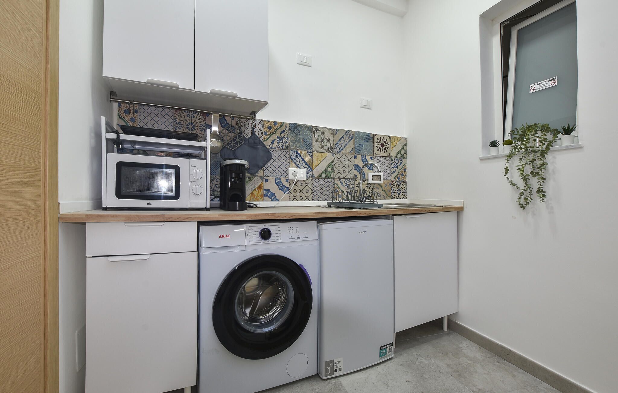 Une cuisine compacte équipée d’un lave-linge, d’un four à micro-ondes et d’une machine à café.