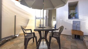 Une terrasse avec une table et des chaises, un grand parasol et un petit coin lavabo.