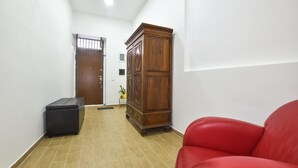 Un couloir avec un meuble en bois, un fauteuil en cuir rouge et un pouf noir.