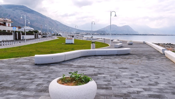 Une promenade en bord de mer, revêtue de pavés, agrémentée de bancs, de lampadaires et d’un panneau indiquant un passage piéton.