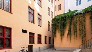 Un patio con una bicicleta, escalones de piedra y un edificio con ventanas de marco rojo y hiedra.