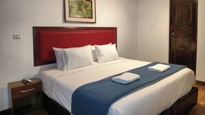 Een net opgemaakt bed met wit- en blauw beddengoed, een rood hoofdeinde en een ingelijste foto erboven.