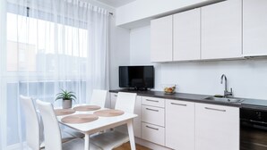 Ett modernt kök med vita skåp, en svart tv och en diskho.