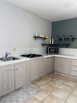 A kitchen with a sink, stove, cabinets, and shelves with decorative items.
