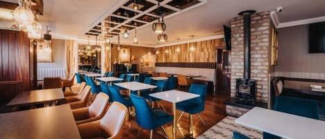 Un restaurante con mesas de madera y sillas azules, una chimenea de ladrillo y lámparas colgantes.
