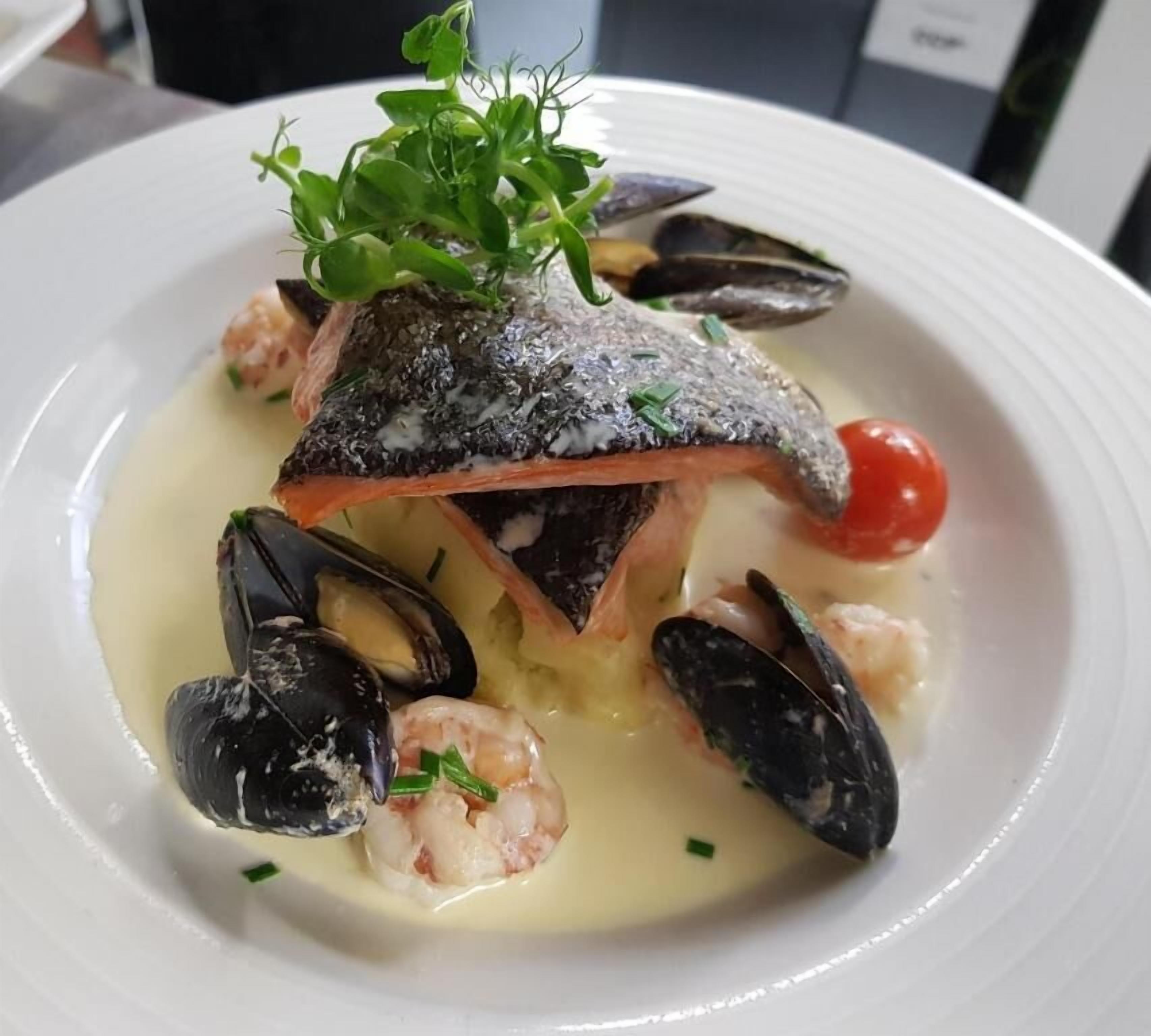 A seafood dish with mussels, shrimp, and a fish on a white plate.