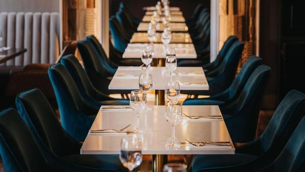 Una sala ristorante con tavoli lunghi e sedie blu scuro, ogni tavolo apparecchiato con bicchieri da vino e posate.