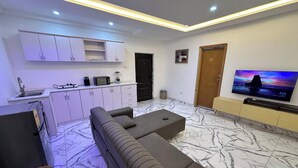 A modern living room with a sofa, TV, kitchen area, and marble flooring. - TN Residence  (Accra)