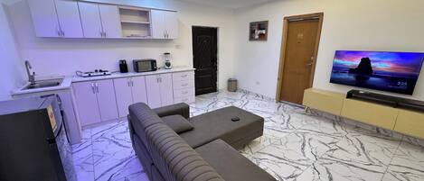 Una sala de estar moderna con sofá, televisión, zona de cocina y suelo de mármol.