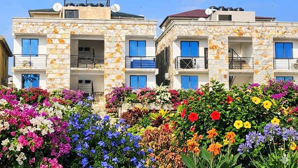A multi-story building with balconies, a stone facade, and a variety of colorful flowers in the foreground. - TN Residence  (Accra)