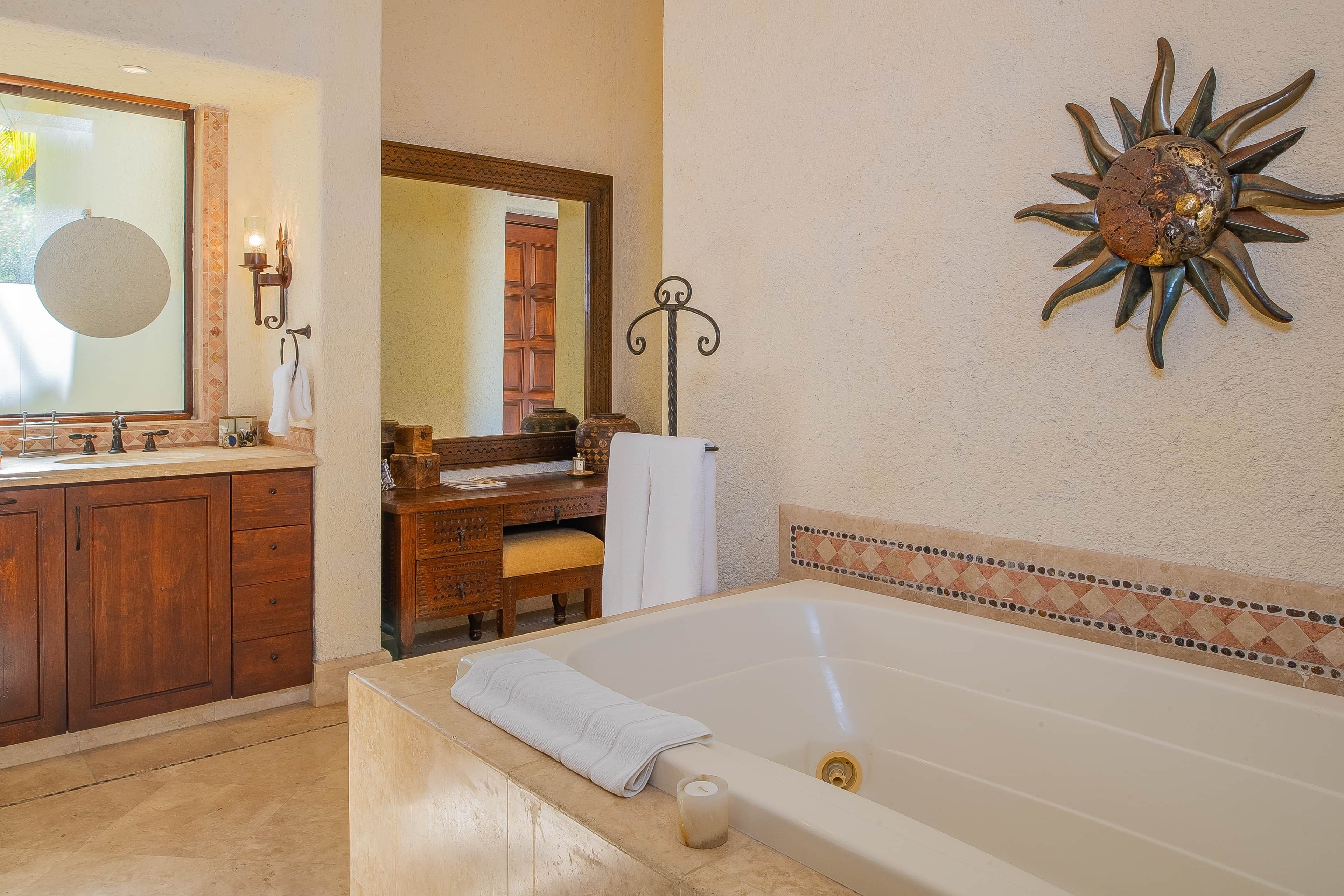 A bathroom with a bathtub, a vanity with a mirror, and a sun-shaped wall decoration.