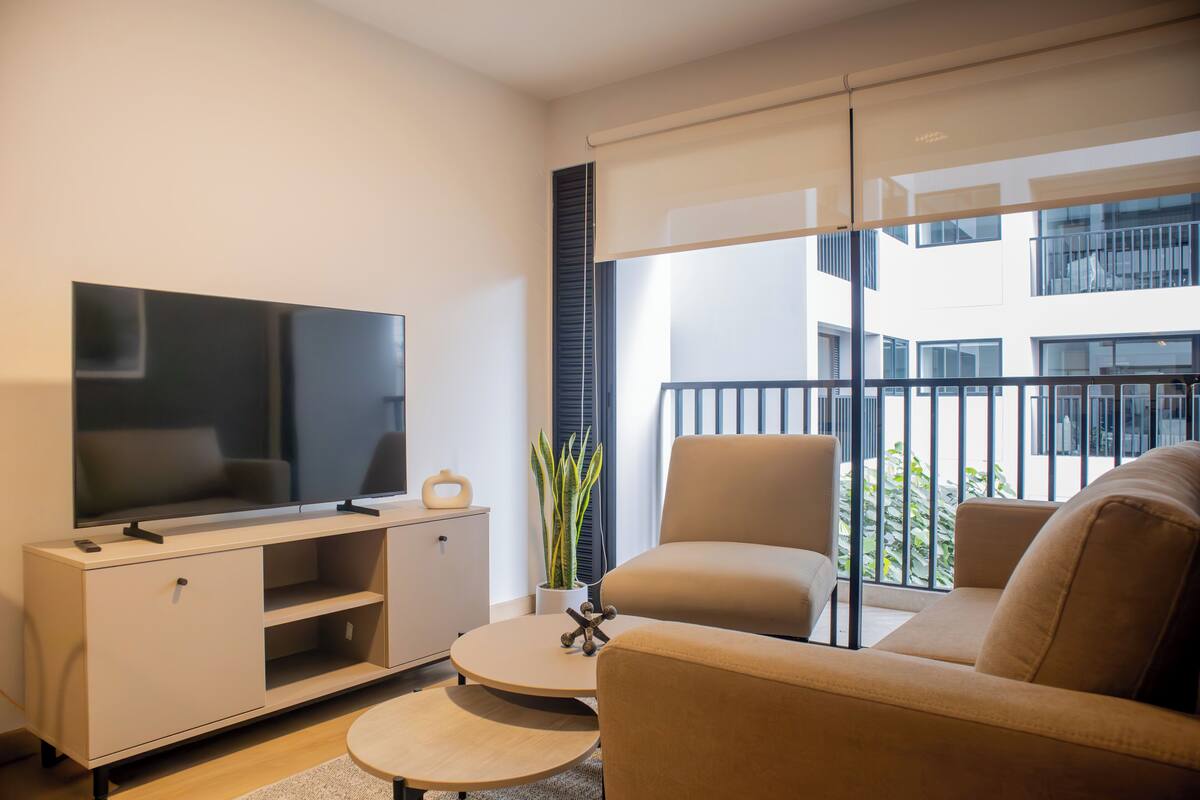 Uma sala de estar moderna com uma televisão de tela plana, um sofá, uma mesa de centro e uma planta em vaso.