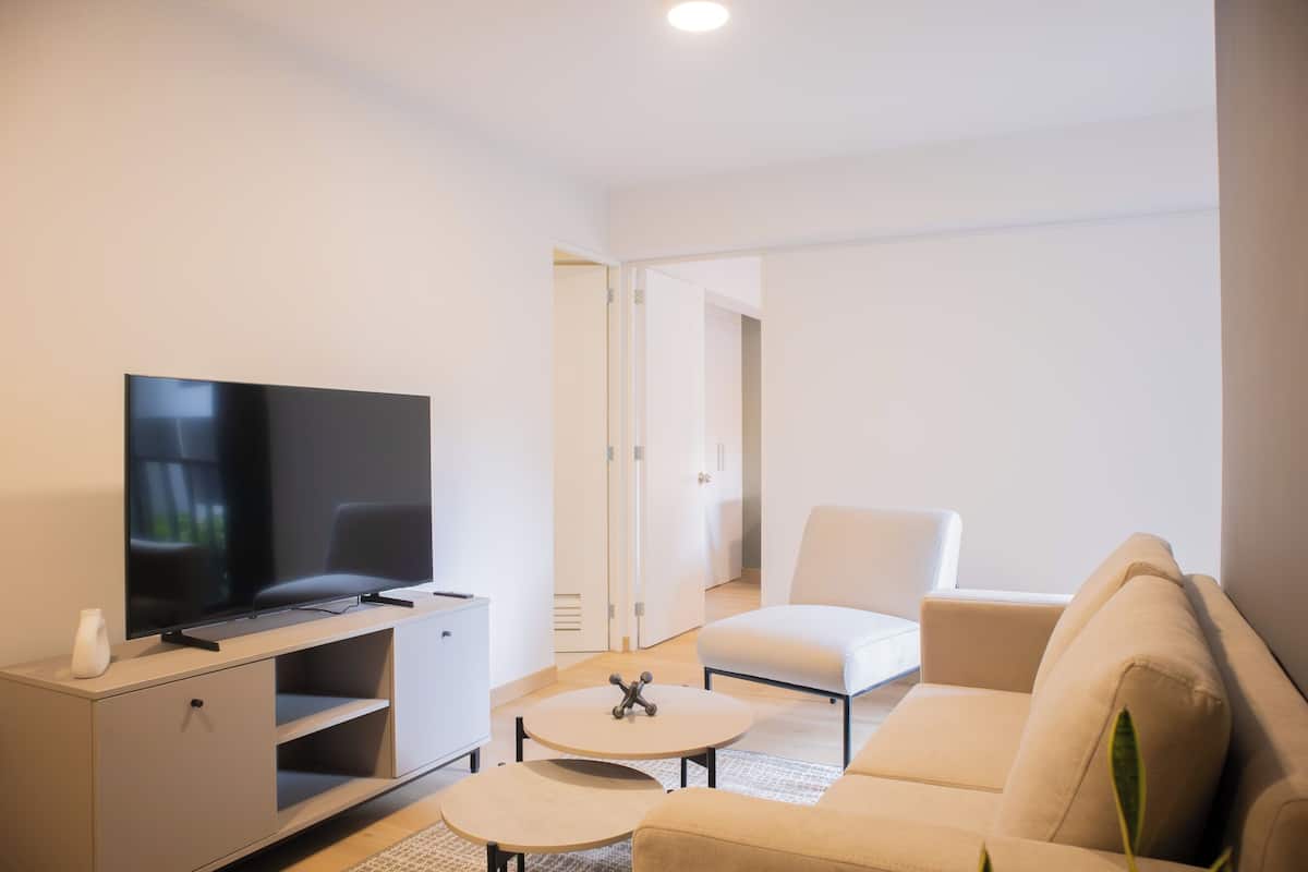 Uma sala de estar moderna com televisão de tela plana, sofá, mesa de centro e poltrona branca.