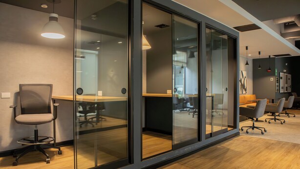 Un espace de bureau moderne avec des cloisons en verre, une table de conférence, des chaises de bureau et un coin cuisine bien visible.