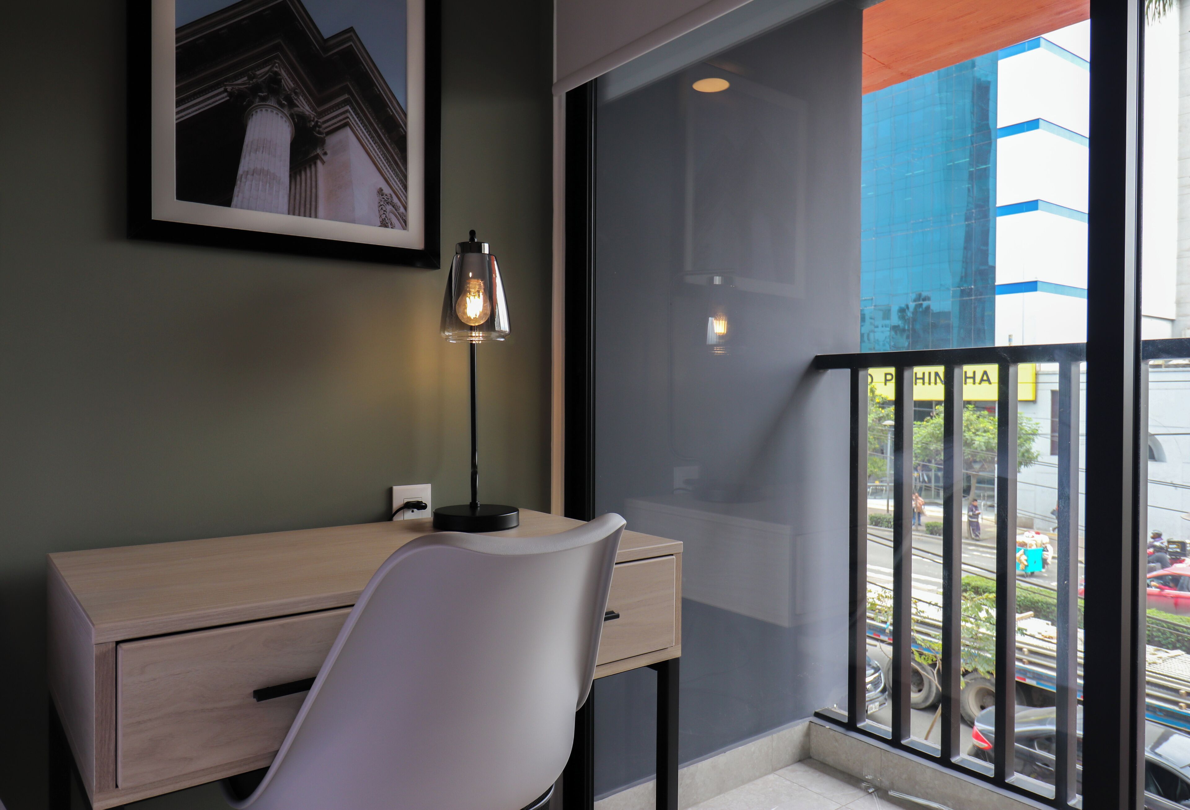 Une chambre moderne équipée d’un bureau, d’une chaise et d’une grande fenêtre donnant sur la rue.