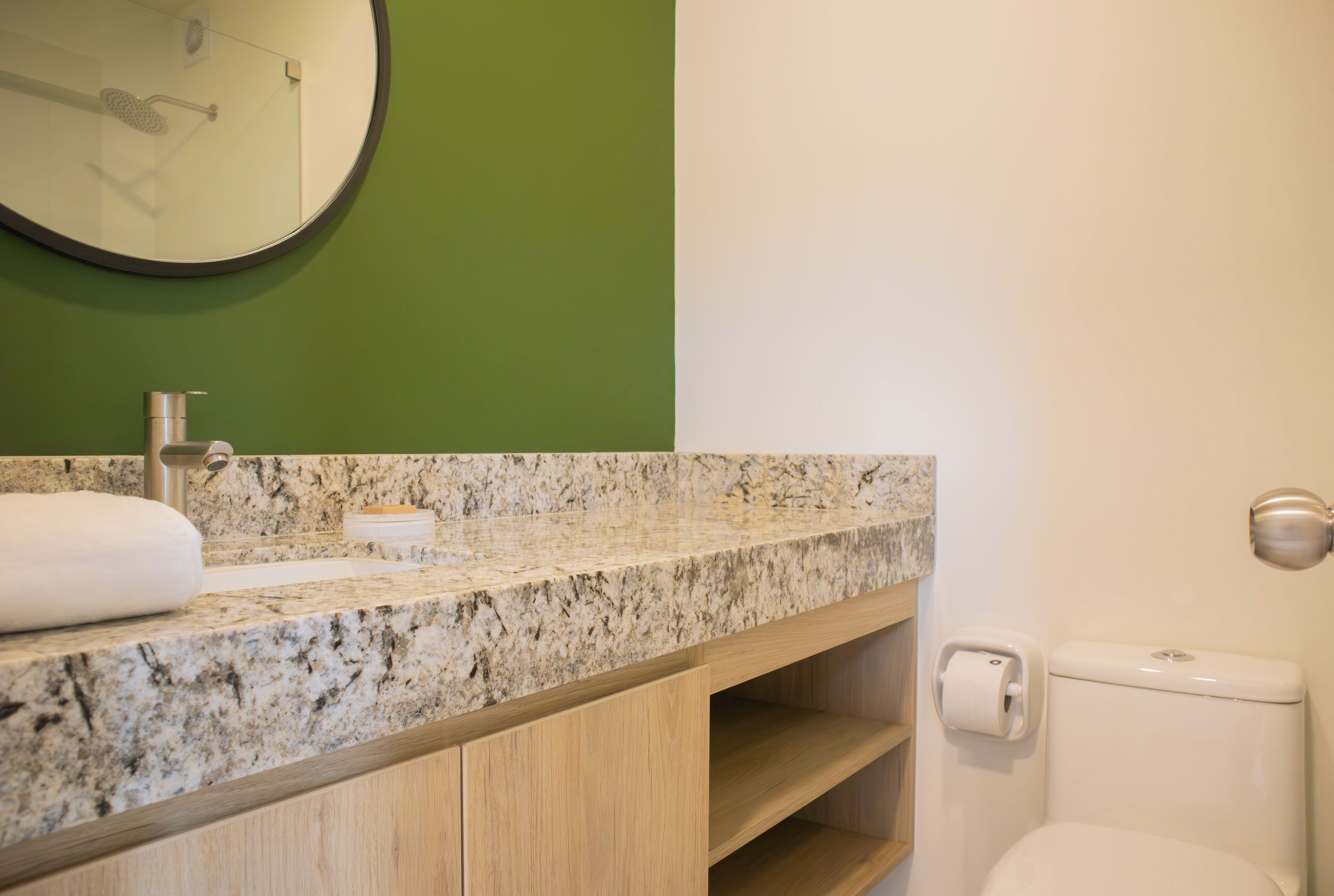 Ein Badezimmer mit einer Granit-Arbeitsplatte, einer Toilette und einer grünen Wand.