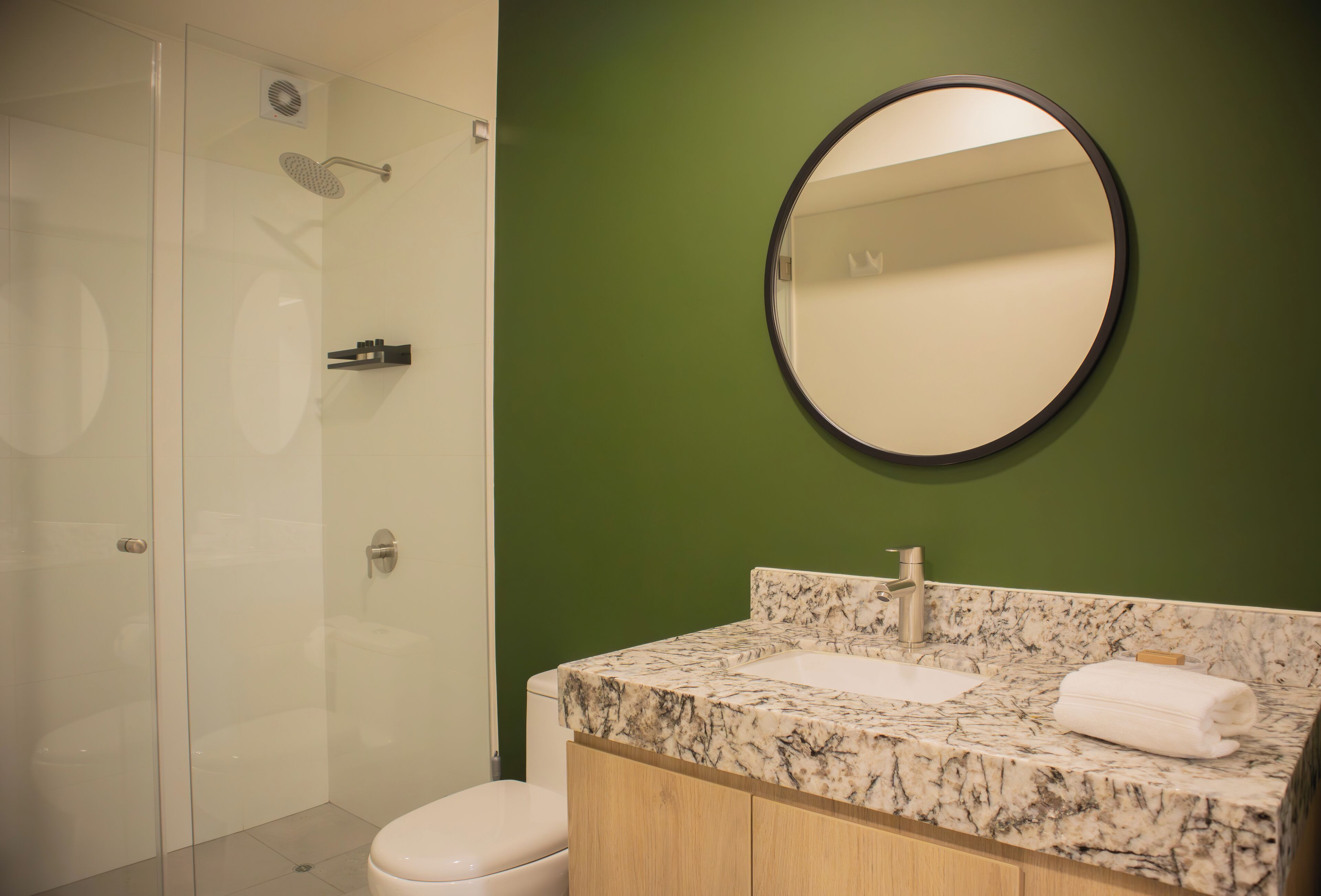 Un baño con cabina de ducha de vidrio, lavamanos de mármol y pared verde.