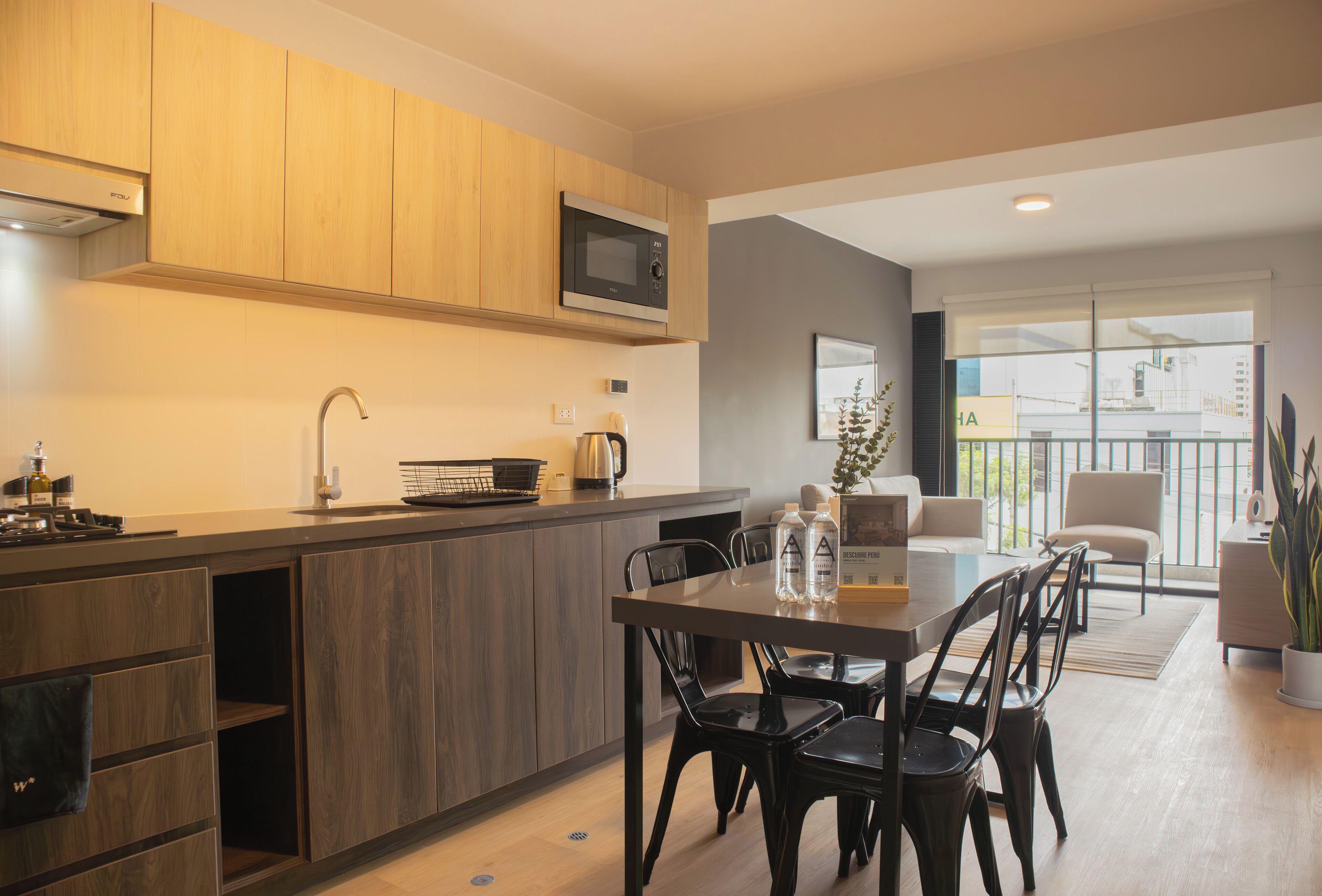 Una cocina moderna con armarios de madera, un microondas integrado y un comedor con mesa y sillas.