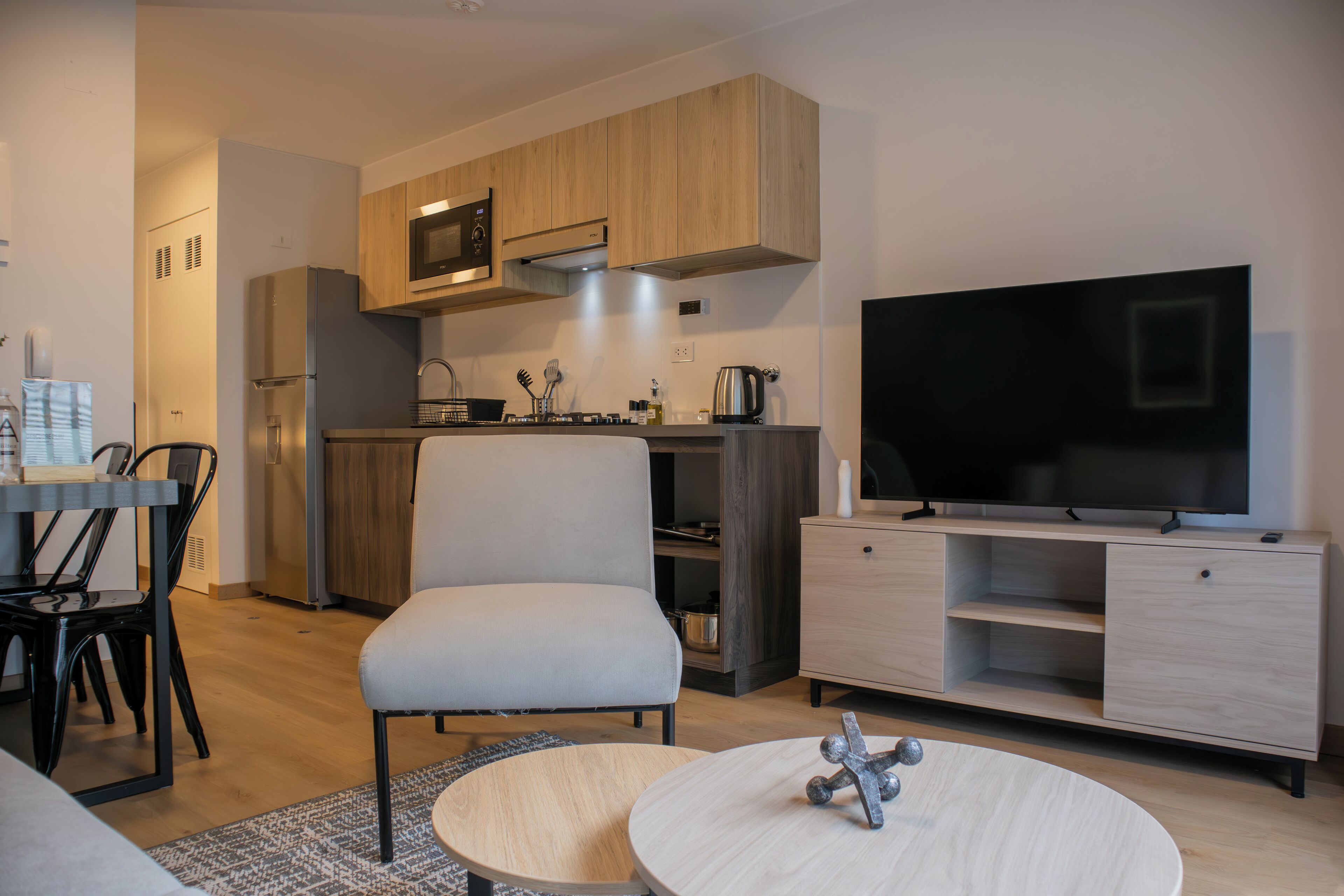 A modern kitchen with wooden cabinets, a built-in microwave, and a large flat-screen TV on a wooden stand.