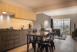 A modern kitchen with wooden cabinets, a dining table with chairs, and a city view through large windows.