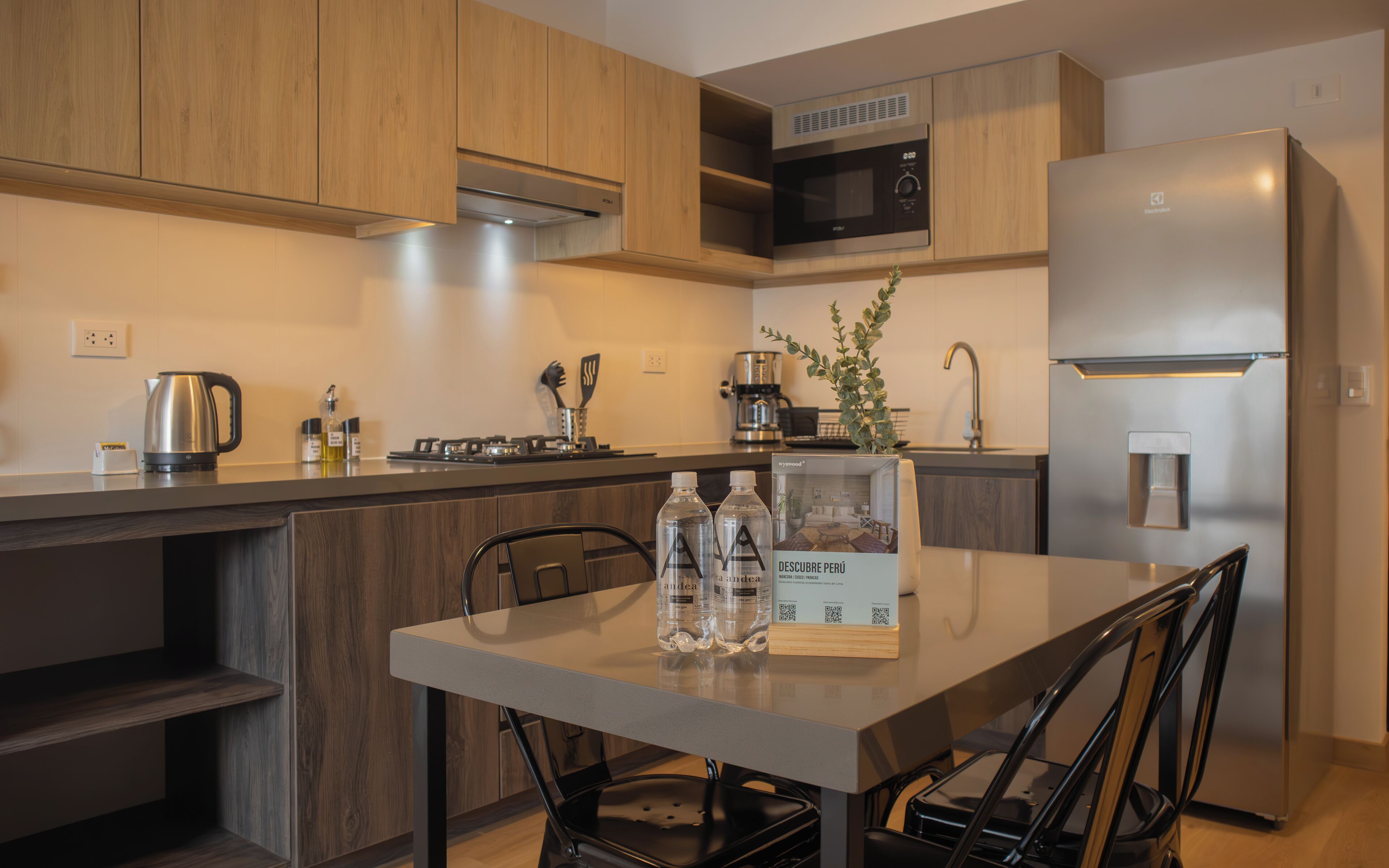 A modern kitchen with wooden cabinets, a stainless steel refrigerator, a built-in oven, and a coffee maker.