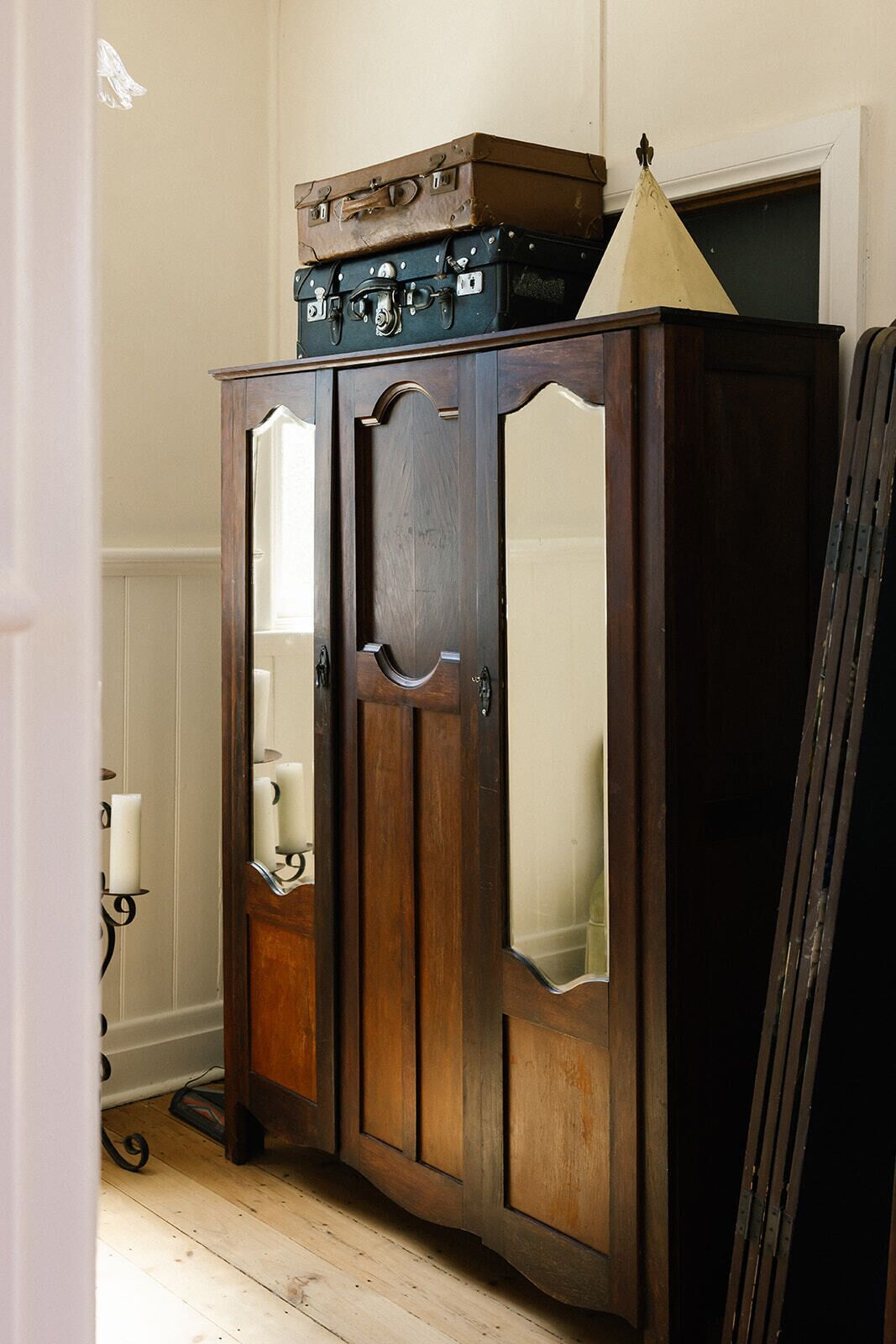 A wooden cabinet with mirrored doors and a top shelf holding suitcases.