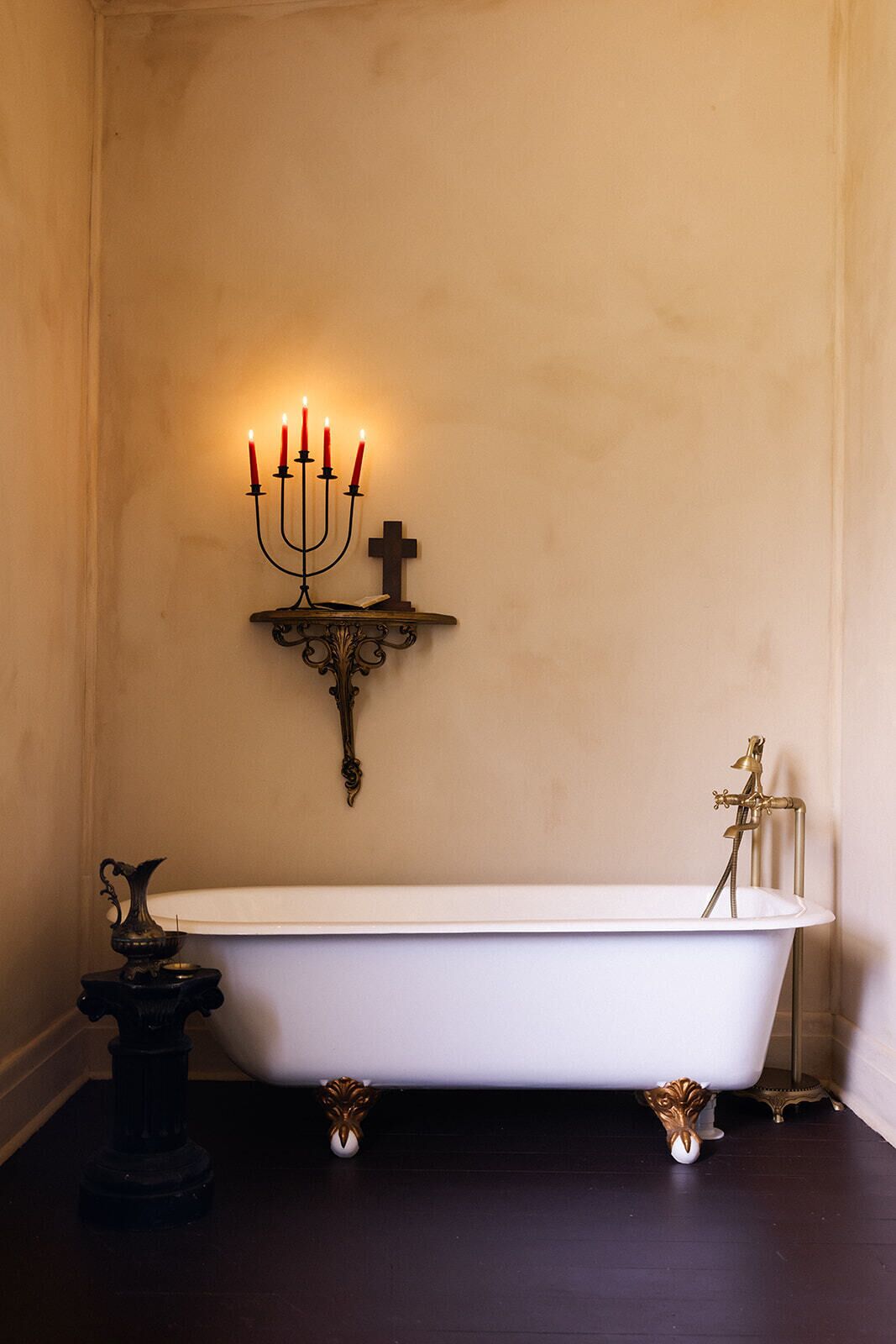 A bathroom with a freestanding bathtub, a wall-mounted candelabra with lit candles, and a small decorative fountain.