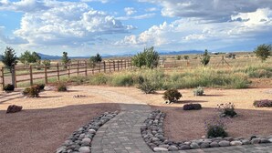 Un camí pavimentat que condueix a una zona tancada amb una base de grava, envoltada de petits arbustos i roques.