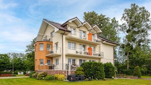 A multi-story residential building with balconies, a patio area with outdoor furniture, and a well-maintained garden.