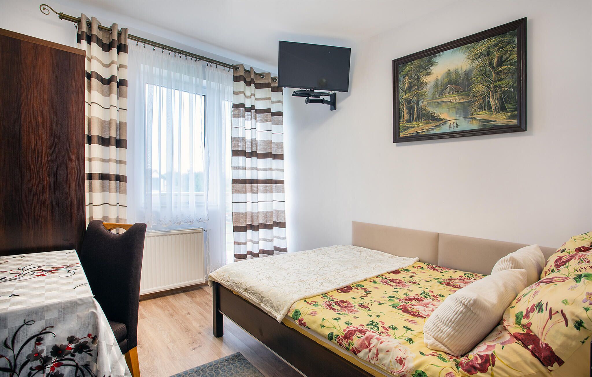 A bedroom with a bed, a chair, a radiator, a painting, and a window with curtains.
