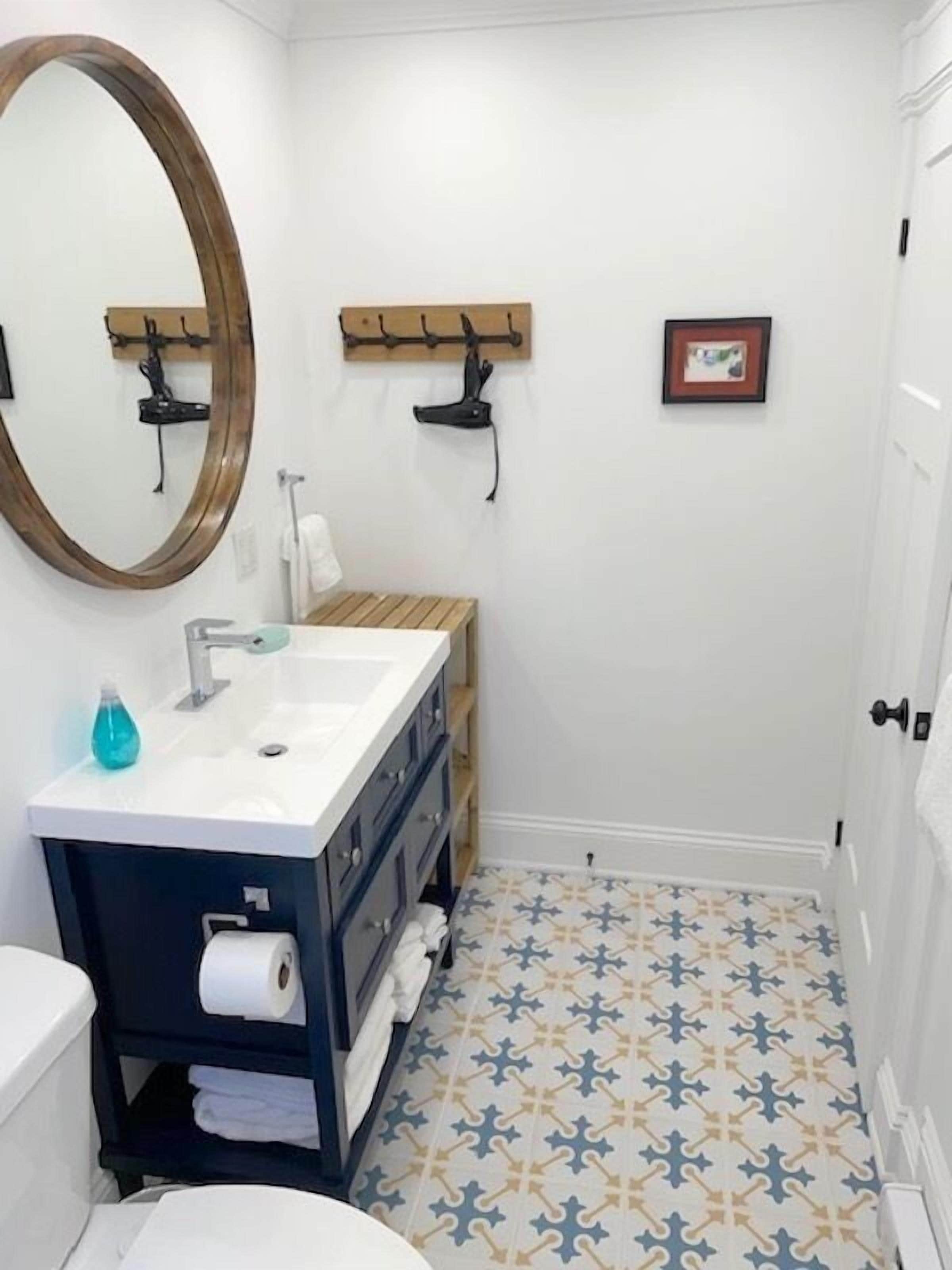 Une salle de bain avec un lavabo blanc, des meubles sombres, un meuble-lavabo en bois, un grand miroir et des carreaux de sol à motifs.