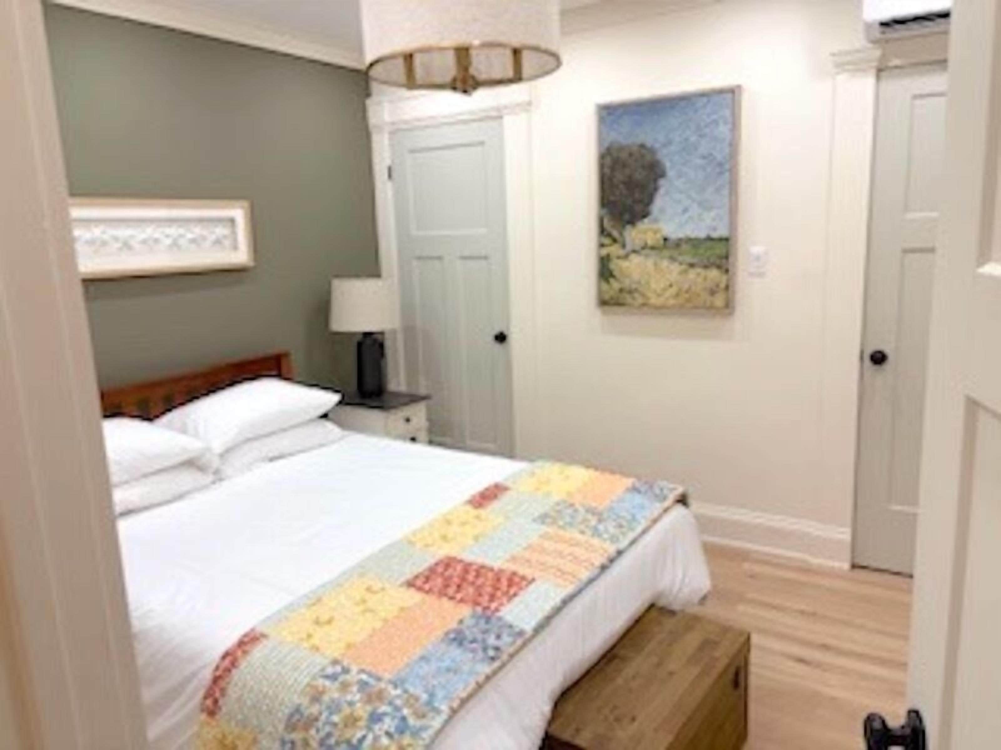 A bedroom with a bed, a nightstand, a lamp, a door, and a painting on the wall.