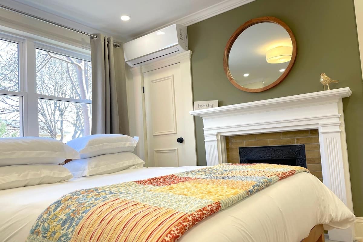 Un dormitorio con cama, chimenea, espejo y ventana con cortinas.