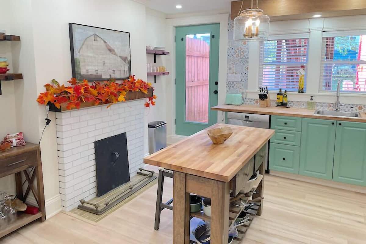 Una cocina con chimenea de ladrillo blanco, una mesa de madera y armarios color turquesa.