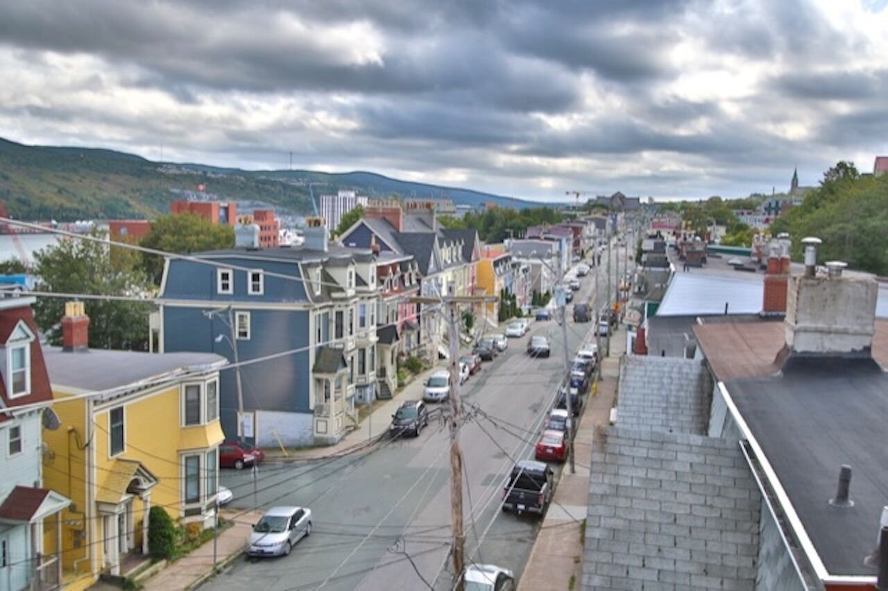 A street view with residential buildings, parked cars, and utility poles.