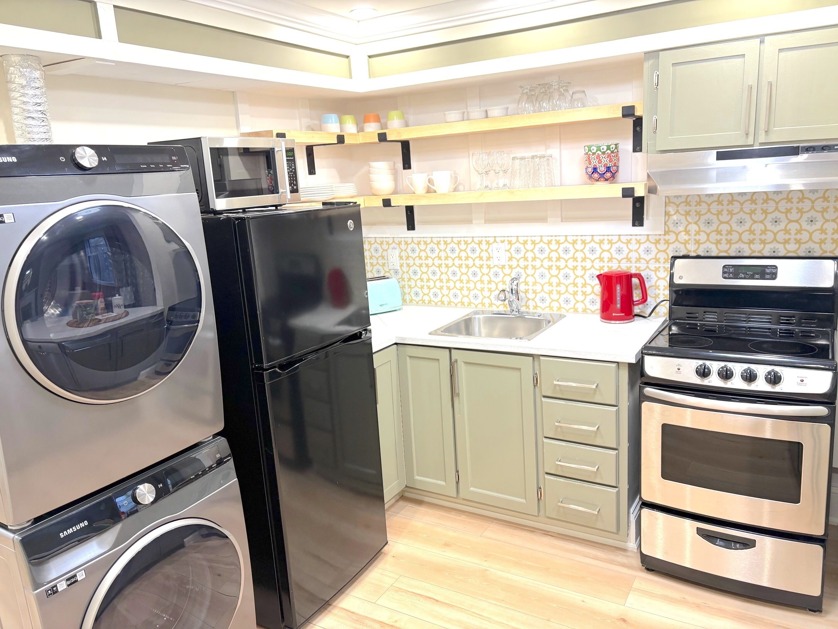 A compact kitchen with a washing machine, a refrigerator, a microwave, a sink, and a stove.