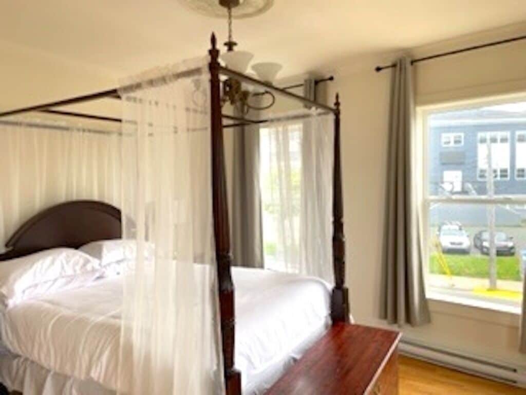 A four-poster bed with white linens, a wooden headboard, and a canopy.