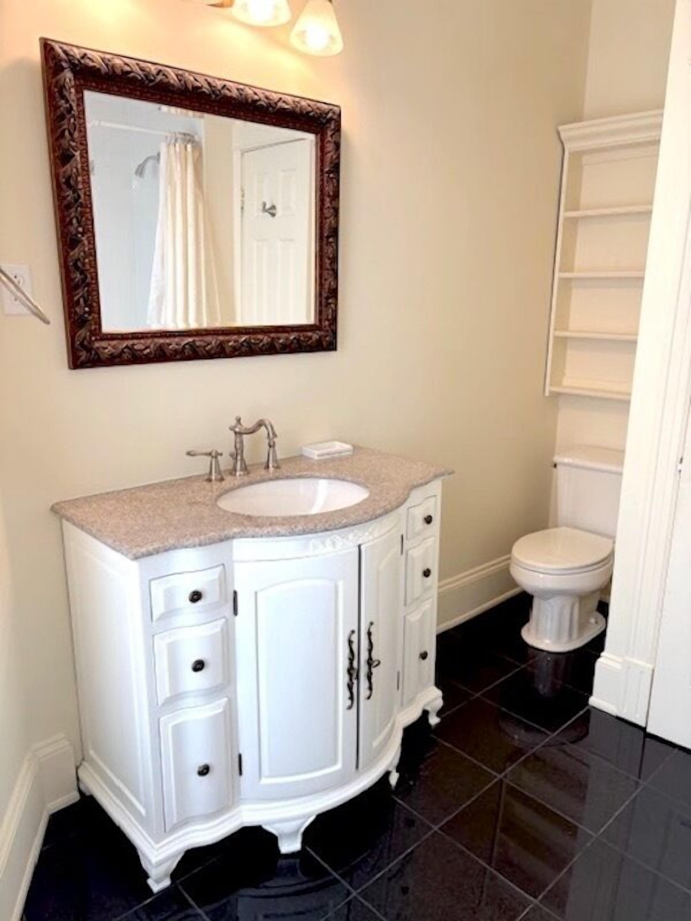 A bathroom with a white vanity, a sink, and a mirror with a decorative frame.