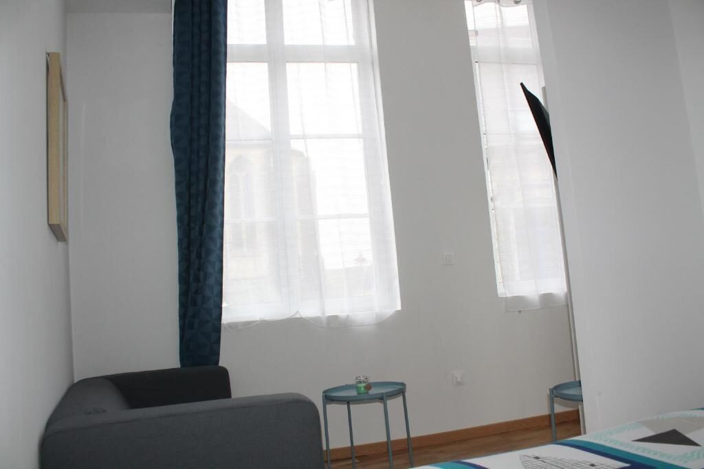 A room with a bed, a chair, two small tables, and a window with curtains.