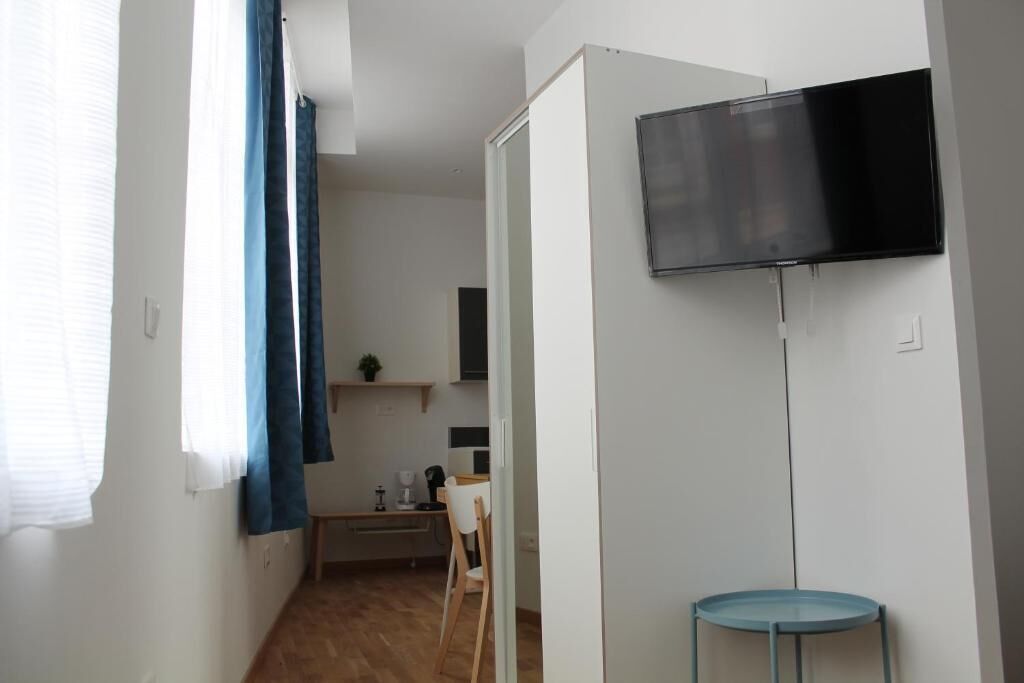 A small, modern room with a flat-screen TV mounted on the wall, a small table, and a chair.