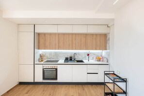 A compact kitchen with white cabinetry, a wooden countertop, a built-in oven, and a black shelf unit.