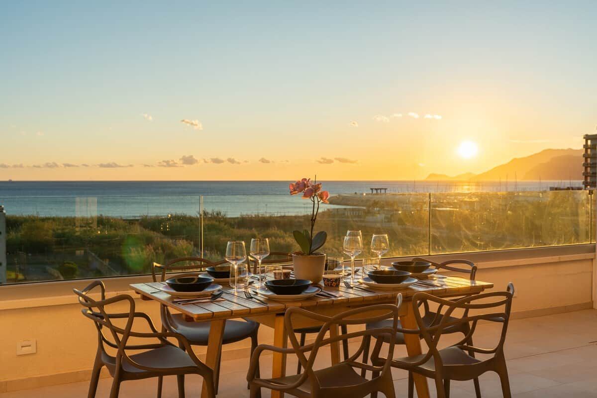 A dining table set for six with a view of the ocean and mountains.
