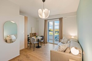 Uma sala de estar moderna com sofá, mesa de jantar e cadeiras. Há uma janela grande com cortinas e vista para o exterior.