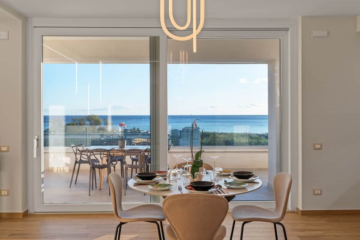A dining area with a view of the sea, a balcony with outdoor seating, and a modern interior design.