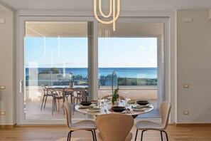 Bright dining area with stunning sea views through large sliding doors. A round table elegantly set for four creates a warm, inviting atmosphere, while the terrace beyond offers the perfect spot for outdoor meals overlooking the blue horizon. - Luxury Sea-View Penthouse - 4BR - Terrace - Arechi (Campania)