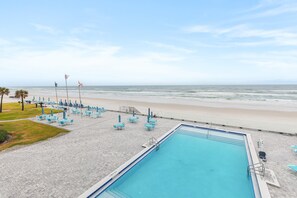 A pool area with a view of the beach, lounge chairs, and flags. - Oceanfront Balcony Condo – Walk to Dining, Splash Park & More (Daytona Beach)