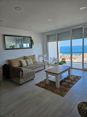A modern living room with a sofa, a coffee table, and a large window offering a view of the sea. - ME&YOU Apartment in Sesimbra , 300 mts from the beach with free parking. (Sesimbra)