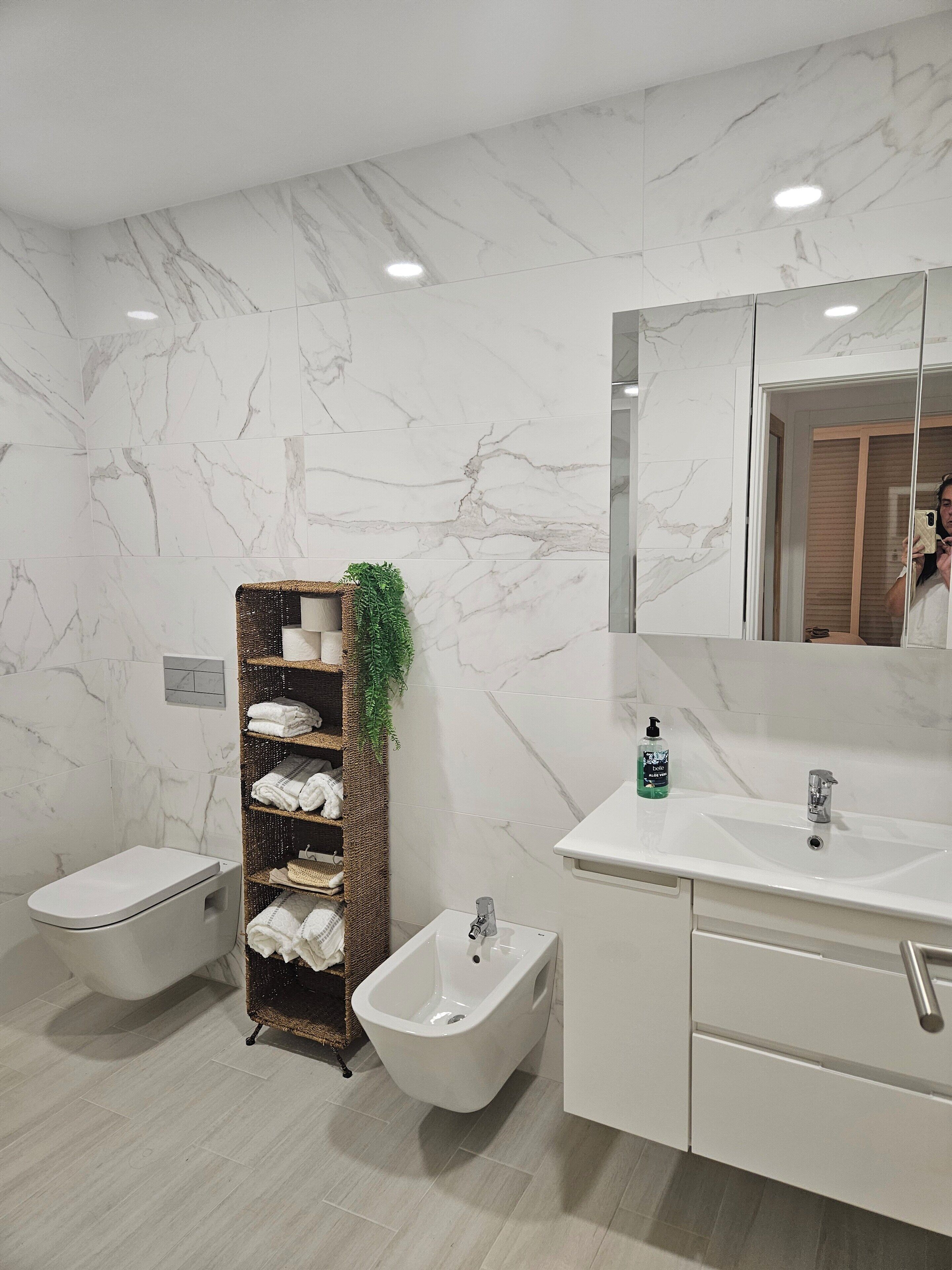 Un baño moderno con un bidé, un tocador con espejo y un estante con toallas.